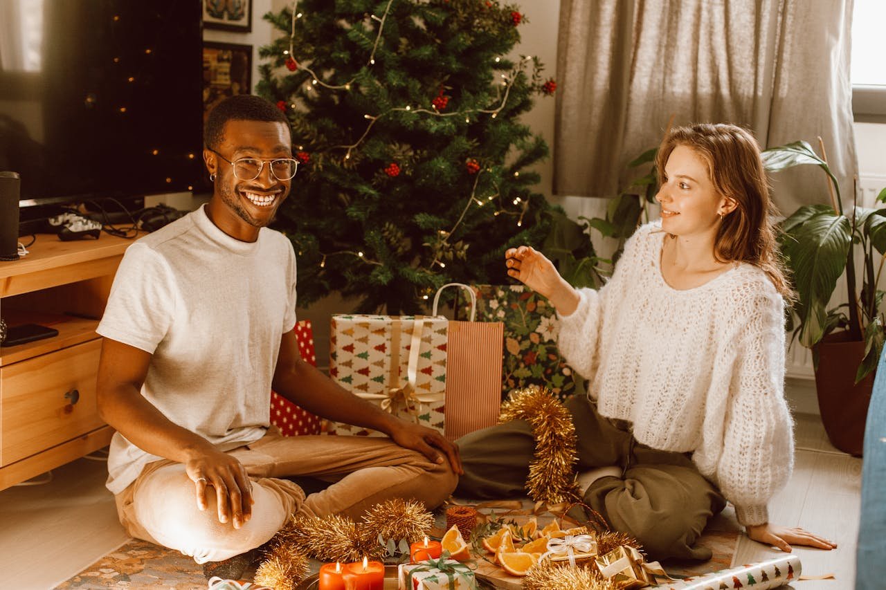 Home Smiling couple enjoying Christmas decorations and gifts by the tree indoors.